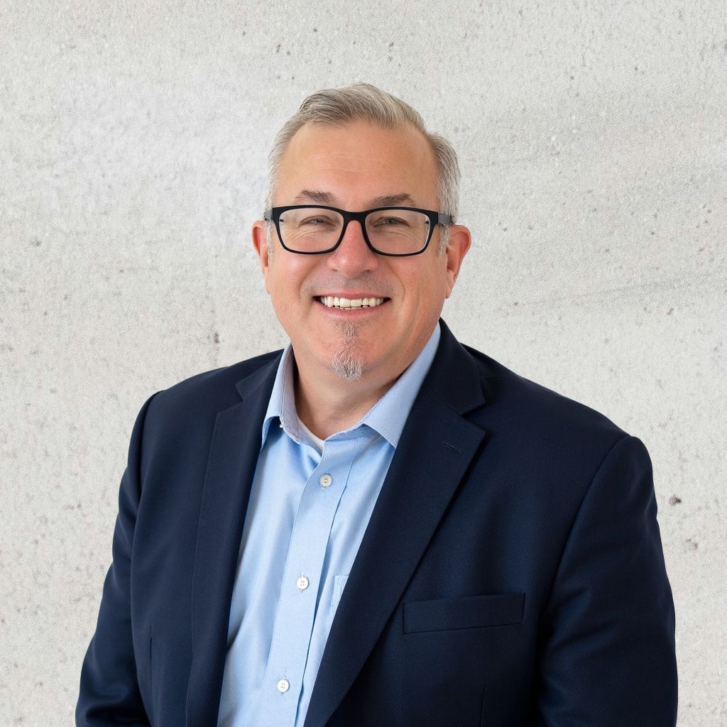 Headshot of Chris Fredrickson, the Chief Operating Officer, wearing glasses, a navy blazer, and a light blue shirt, smiling warmly against a light textured background.