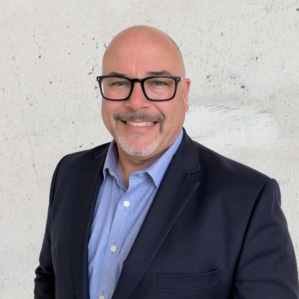 Headshot of Justin Gauthier, Director of Operations and Technical Solutions Canada, wearing a blue blazer and blue shirt, smiling confidently against a light textured background.