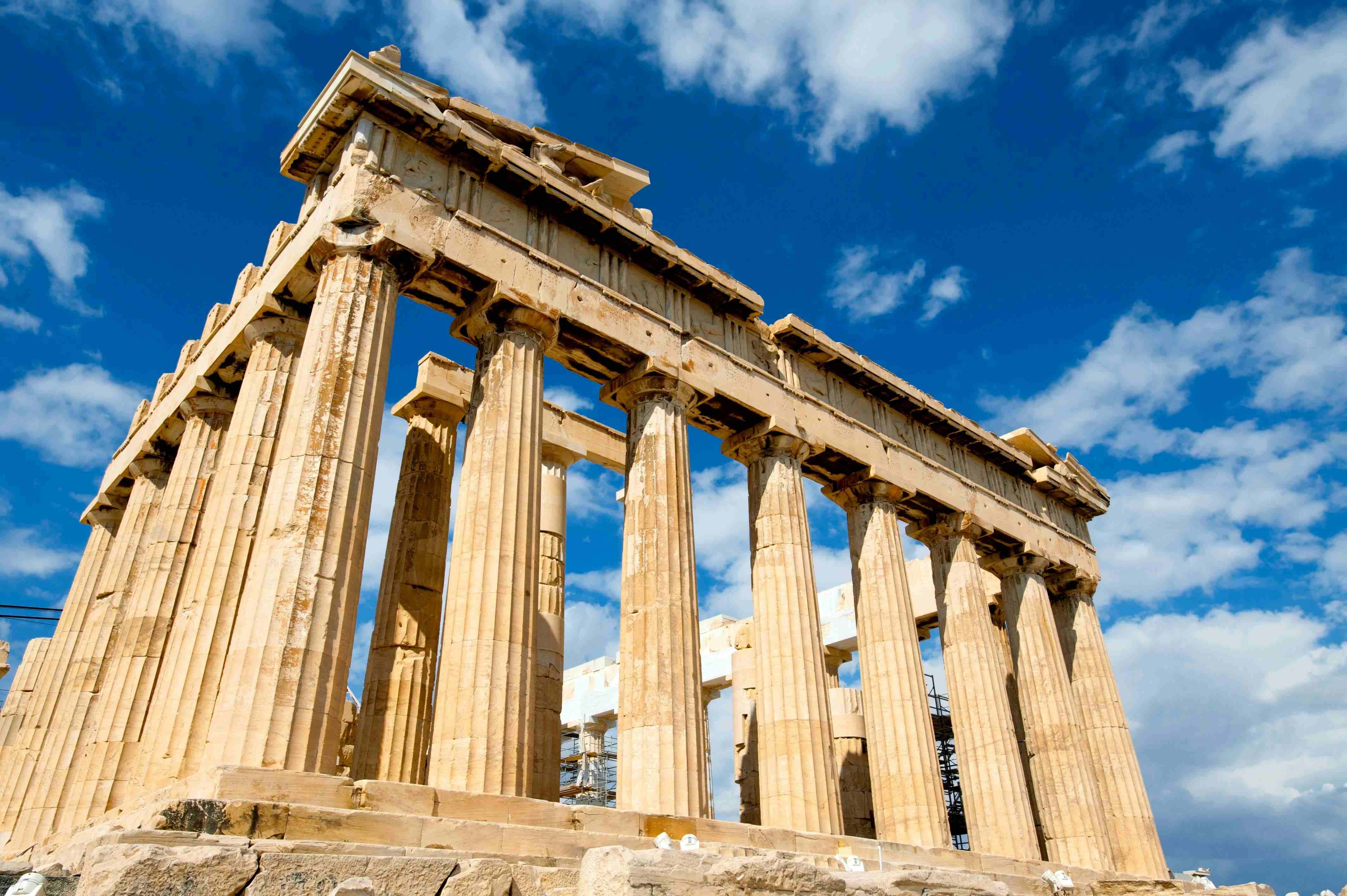 The Greek Parthenon against a bright blue cloudy sky.