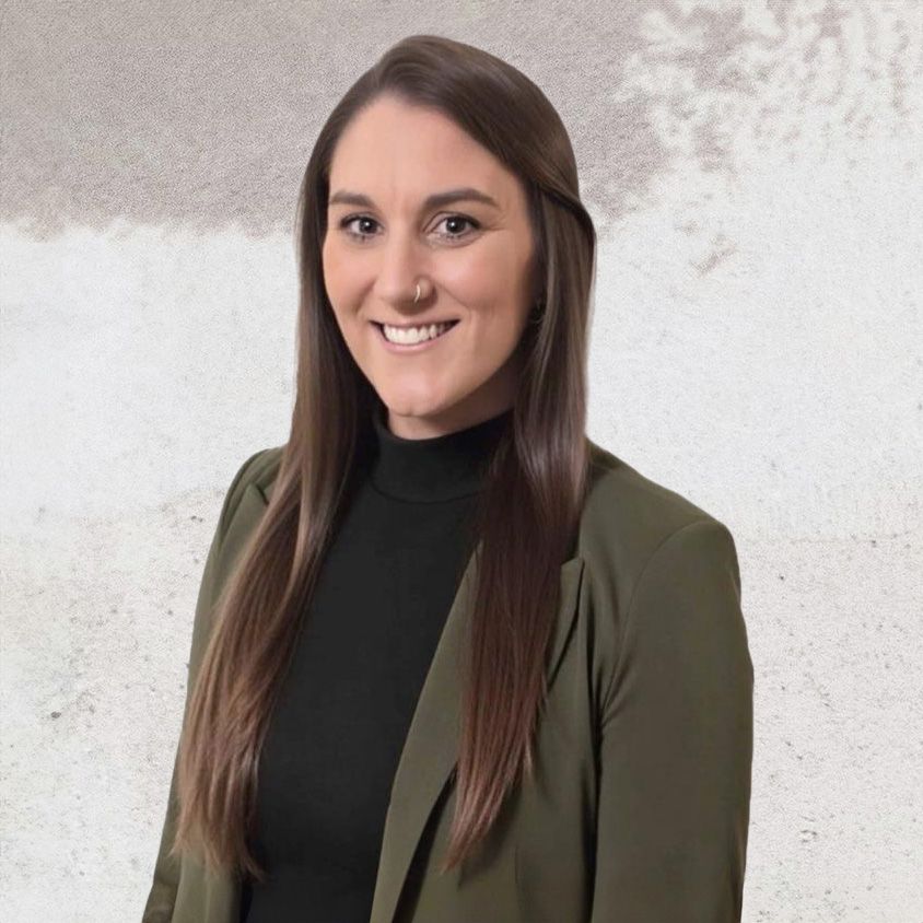 Jenni Yearta, Director of Accounting and Human Resources, posing for a professional headshot against a textured white background, wearing a green blazer and black turtleneck.